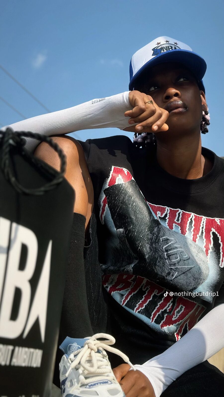 Close-up of a model in the black graphic tee and blue trucker cap, holding an NBA shopping bag