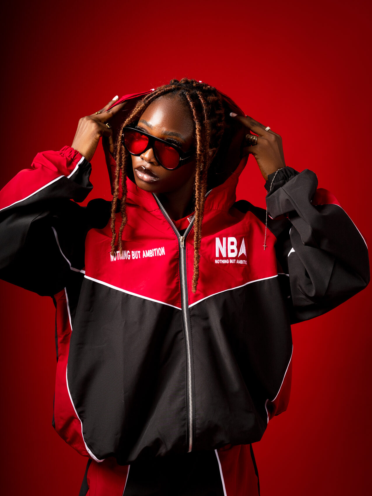 Model wearing the red and black performance tracksuit with the hood up, on a red studio backdrop