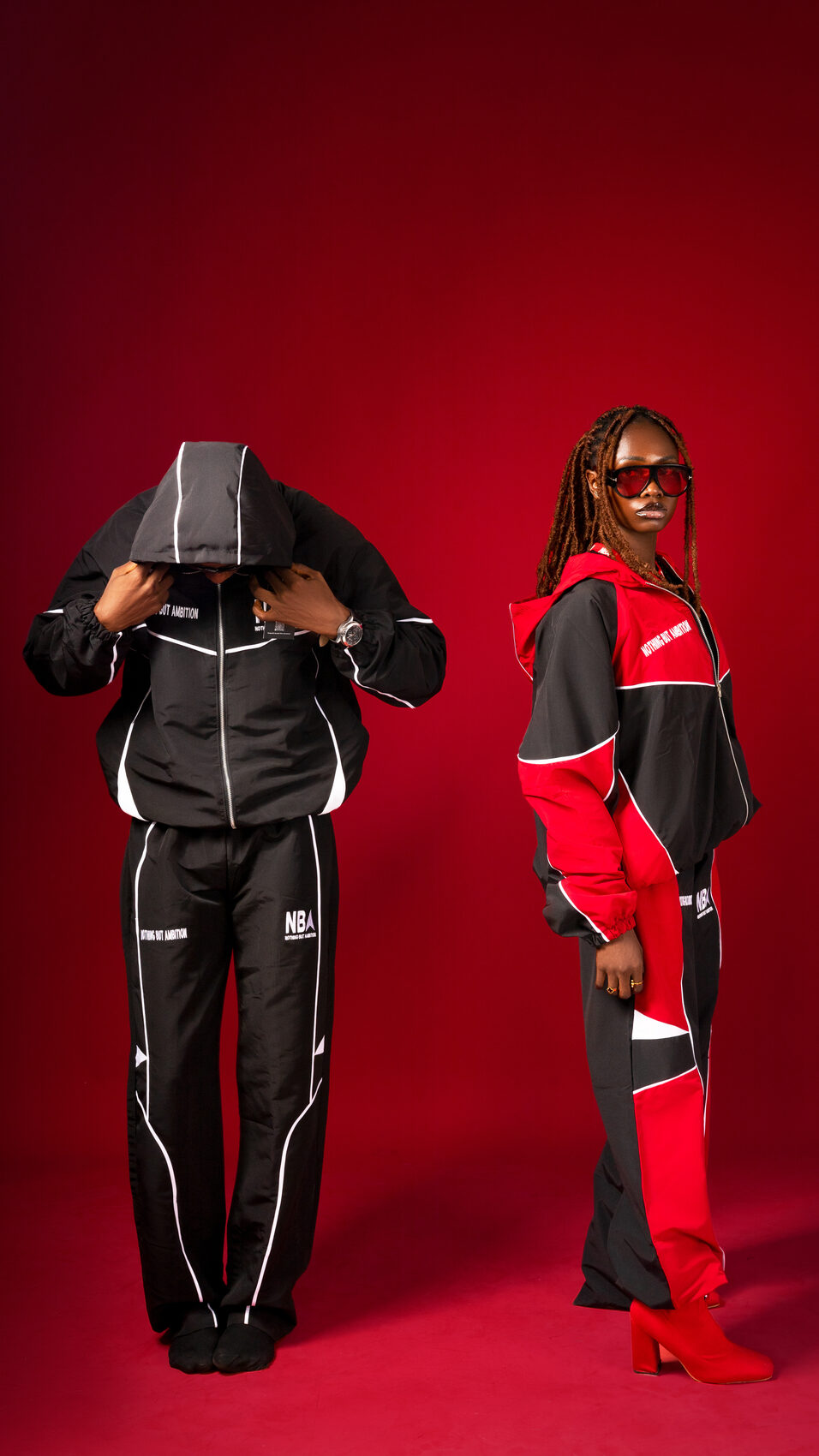 Two models wearing NBA tracksuits in black and red/black, studio shot on red backdrop