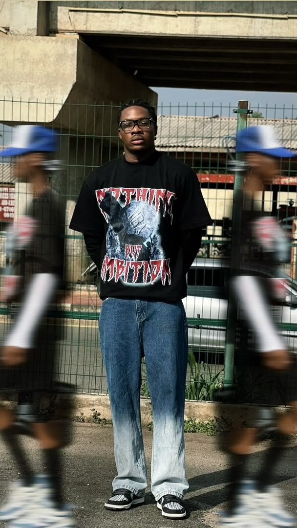 Model wearing the black NBA graphic tee and glasses, artistic motion-blur effect, blue trucker caps either side