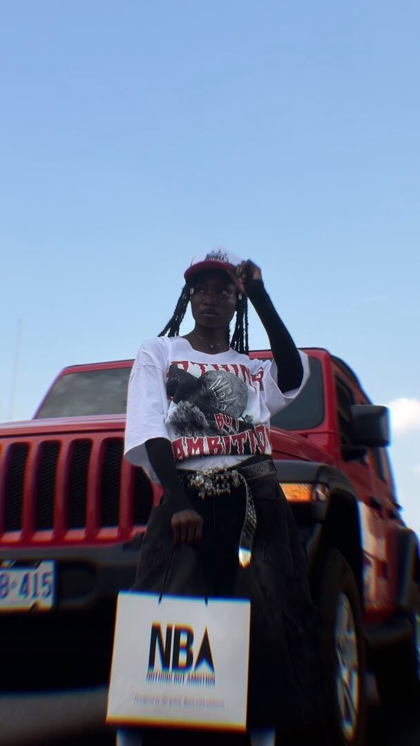 Model wearing the white NBA graphic tee and red trucker cap, standing beside a red Jeep