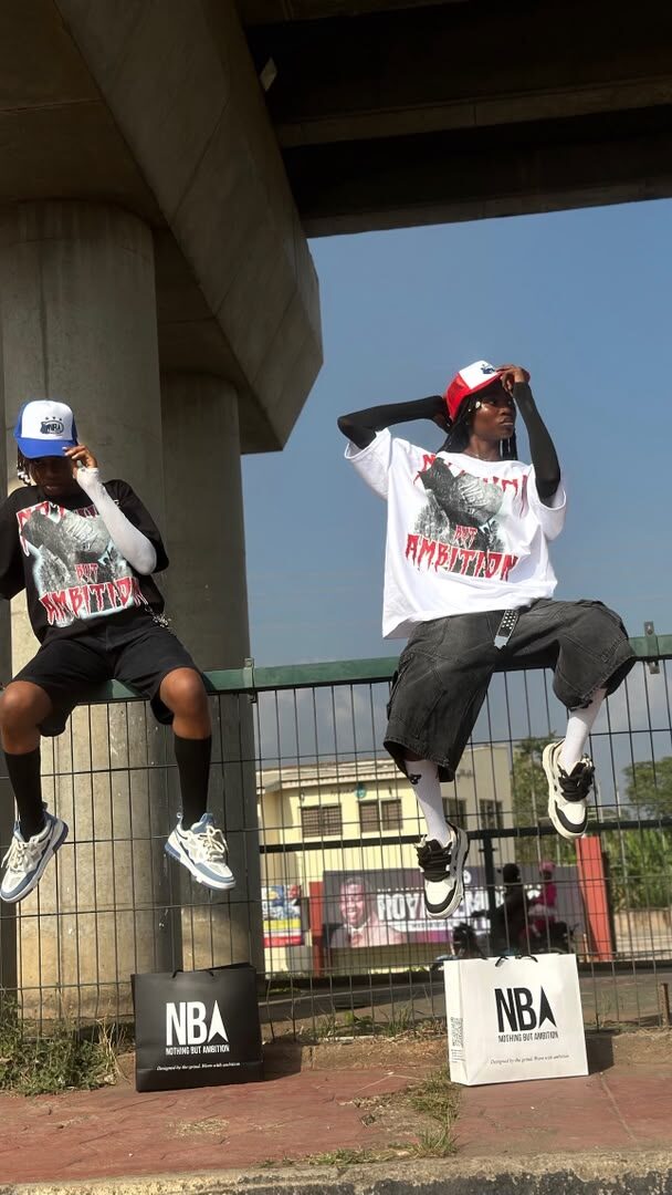 Two models jumping mid-air under a city overpass, wearing NBA graphic tees and trucker caps, NBA shopping bags on the ground